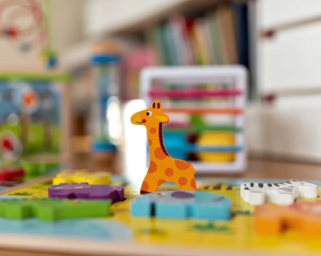 Focus shot of cartoon giraffe puzzle piece standing up with other animal puzzle pieces laying down. Inside of classroom with books and other educational toys.